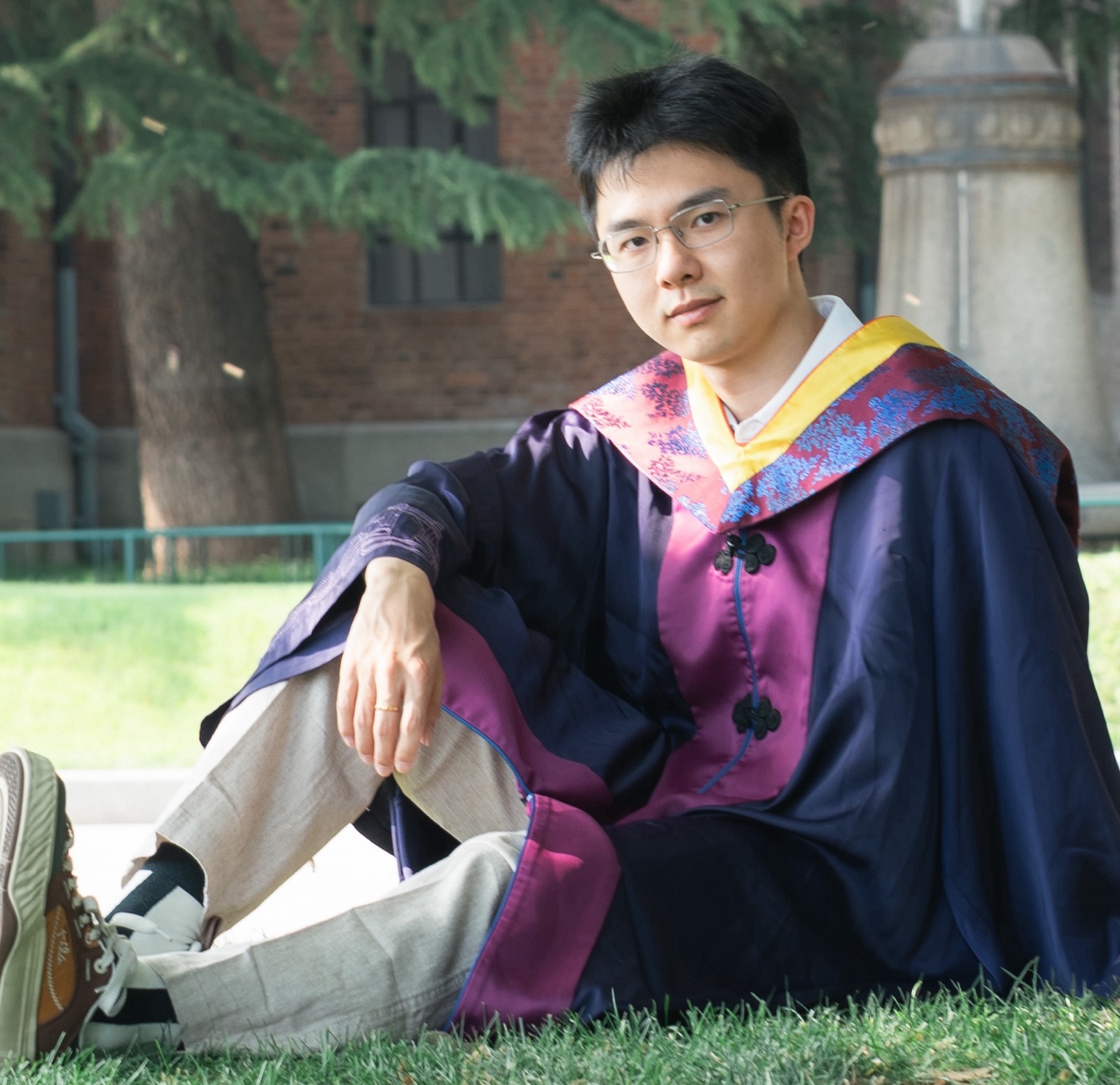 Junlin Yang in academic dress, sitting on the lawn